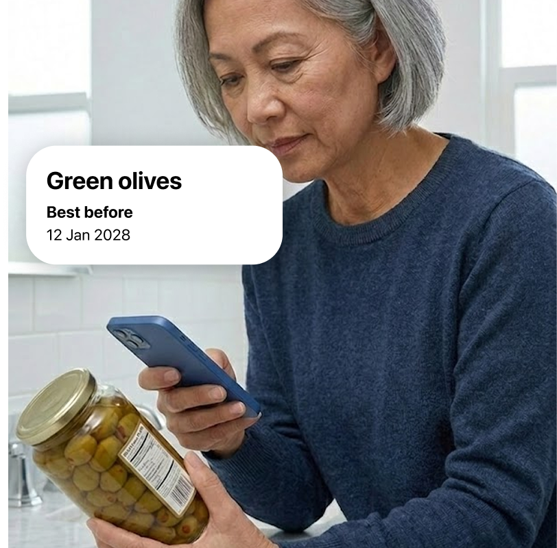 An older woman scans a glass jar of olives with her smartphone. The app overlay reads: Green olives. Best before: 12 Jan 2028.